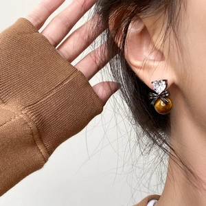 Close-up of elegant tiger eye heart earrings with black bow detail worn by a model