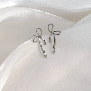 Elegant silver bow stud earrings resting on luxurious white silk fabric backdrop