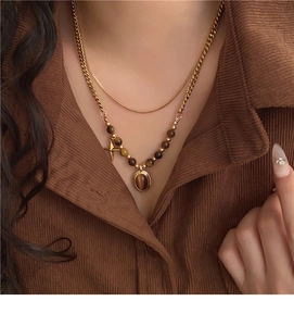 Close-up of double-layer gold necklace with tiger eye beads and oval stone pendant