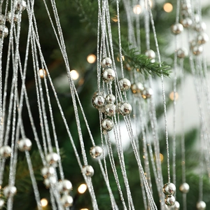 Guirlande de perles argentées pour sapin de Noël sur branches vertes avec lumières chaudes