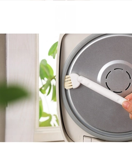 Macro view of a 90-degree rotating cleaning brush scrubbing an electric cooker lid gap