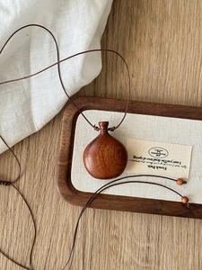 Detail of a dark brown wooden bottle pendant with natural wood grain on a braided cord