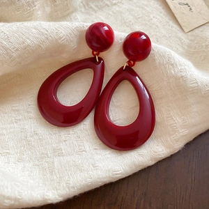 Close-up of red resin teardrop earrings on textured fabric with elegant gold accents