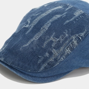 Detailed close-up of dark blue denim beret showing heavy distressed textures and ripped details