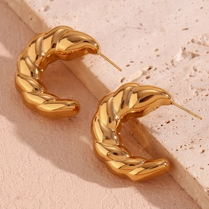 Macro shot of 18K gold plated croissant hoop earrings on beige stone texture