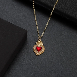 Macro shot of gold-plated necklace with red ruby heart crown pendant on black surface