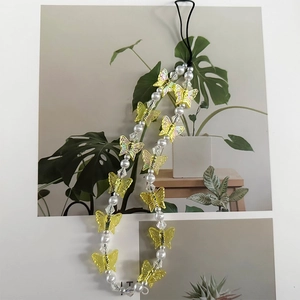 Detail of yellow transparent butterfly bead and white pearls on the colorful phone strap