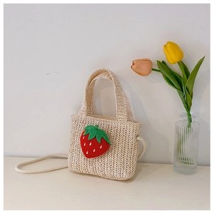 Detail of a beige woven straw bag for children featuring a cute red strawberry ornament