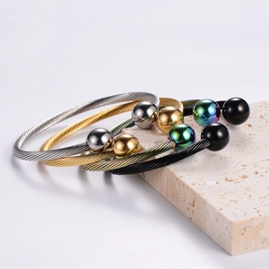 Detail of twisted cable bangles in gold, silver and black finishes on a stone base