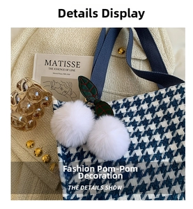 Detail show of houndstooth tote bag featuring soft white fur balls and leather leaf decor