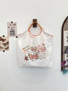 Detail of embroidered floral tote bag with heart patterns and woven orange handles
