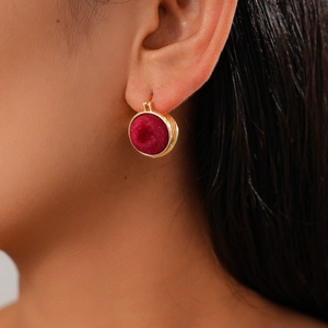 Close-up of a vintage golden round earring with red velvet inlay worn by a model