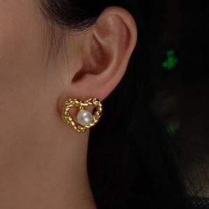 Élégantes boucles d'oreilles cœur dorées avec perle blanche portées par un mannequin
