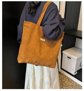 Detail showing ginger yellow corduroy tote bag worn on shoulder in a minimalist setting