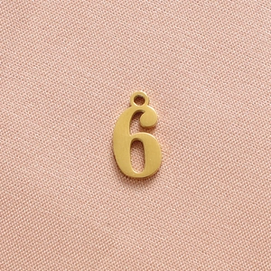 Polished gold number 6 pendant for DIY jewelry on textured pink fabric background