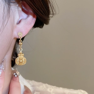 Close-up of a model wearing hollow gold lantern earrings with intricate floral details