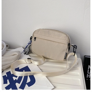 Détail du sac bandoulière en nylon beige avec étiquette mode et breloque en damier
