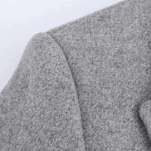 Detailed close-up of grey tweed fabric texture and precise shoulder seam craftsmanship