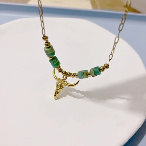 Close-up of golden necklace with green cylindrical beads and ox skull pendant detail