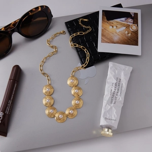 Flat lay of gold stainless steel pearl necklace with coin pendant on laptop background