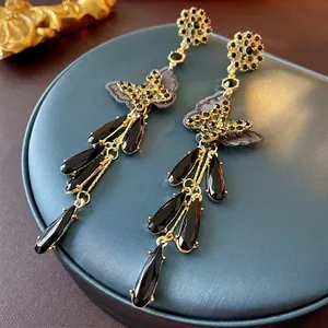 Elegant black bow drop earrings with long tassels and crystal flower studs on a pedestal