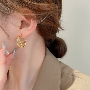 Macro shot of gold C-shaped hoop earrings with cutout letter design on female model