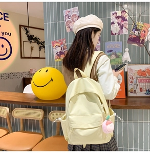 Detail of light yellow nylon backpack with a pink peach plush charm on a wide shoulder strap