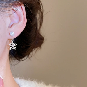 Detailaufnahme eines silbernen Schneeflocken-Ohrrings mit Perlenstecker am Modellohr