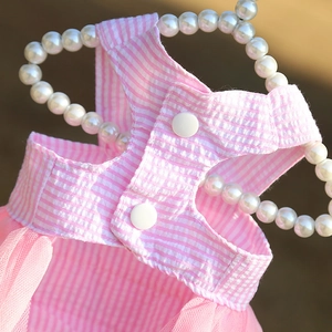 Detail of pink striped pet dress with mesh hem and snap buttons on a pearl hanger