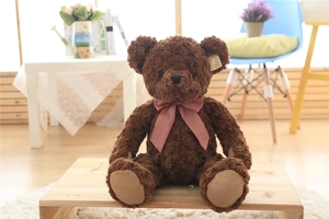 Detailed view of plush dark brown teddy bear skin with soft curly fur and red checkered bow