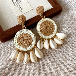 Detail shot of raffia woven earrings with seashell pendants and golden metal accents