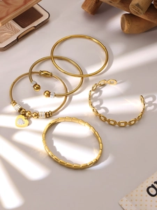 Detalle de cinco brazaletes de acero inoxidable dorado con colgante de corazón
