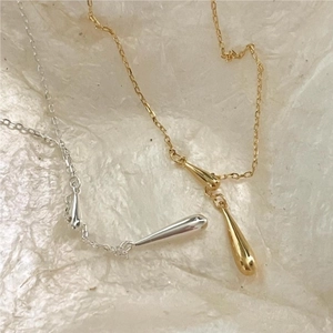 Macro detail of polished teardrop pendants in gold and silver finish on a textured fabric