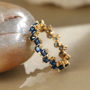 Macro detail of gold-plated ring with princess-cut blue zircons on sandy stones