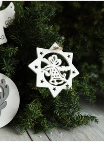Detail of white star wooden Christmas ornament with bell carving hanging on a pine branch