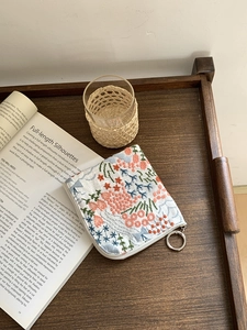 Linen embroidered floral coin purse with metal zipper on a rustic wooden tray