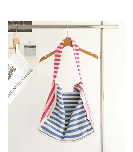 Dettaglio di borse tote in tela a righe blu e rosa appese a una gruccia di legno naturale