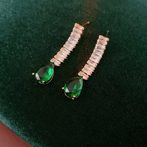 Luxury gold drop earrings with square zircons and pear-shaped green stones on velvet