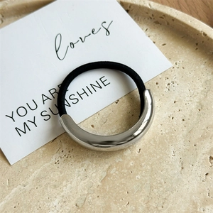 Close-up of minimalist silver metal hair tie on a beige stone tray with a white card
