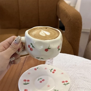 Hand-painted ceramic coffee cup with cherry pattern and heart latte art detail