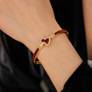 Detail eines vergoldeten Hulu-Armbands mit roter Emaille und Zirkonia am Handgelenk einer Frau