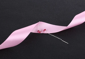 Detail view of silver tassel earrings with red zircon stones on pink silk ribbon