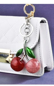 Detailed view of red and pink sequin cherry keychain on a white quilted handbag