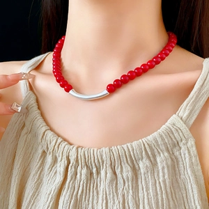 Collier ethnique avec perles rouges et tube argenté courbé sur le cou d'un modèle