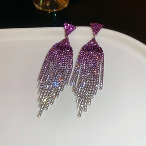 Macro shot of long fringe earrings featuring purple gradient rhinestones and starburst sparkles