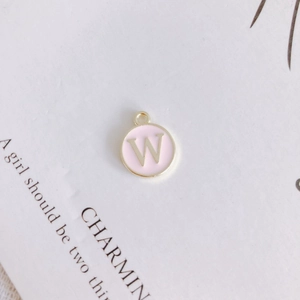 Macro view of a round pink enamel pendant with gold letter W for DIY jewelry making