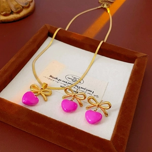 Vue détaillée de la parure dorée avec nœud et cœur magenta, collier et boucles