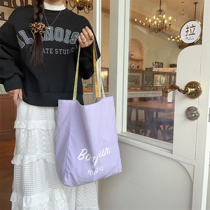 Action shot of a lavender canvas tote bag with Bonjour magic print and plaid handles