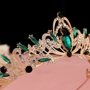 Detailed close-up of vintage golden bridal crown with emerald green gems and rhinestones