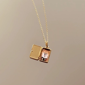 Detail of a gold rectangular locket necklace featuring an open photo compartment with a dog